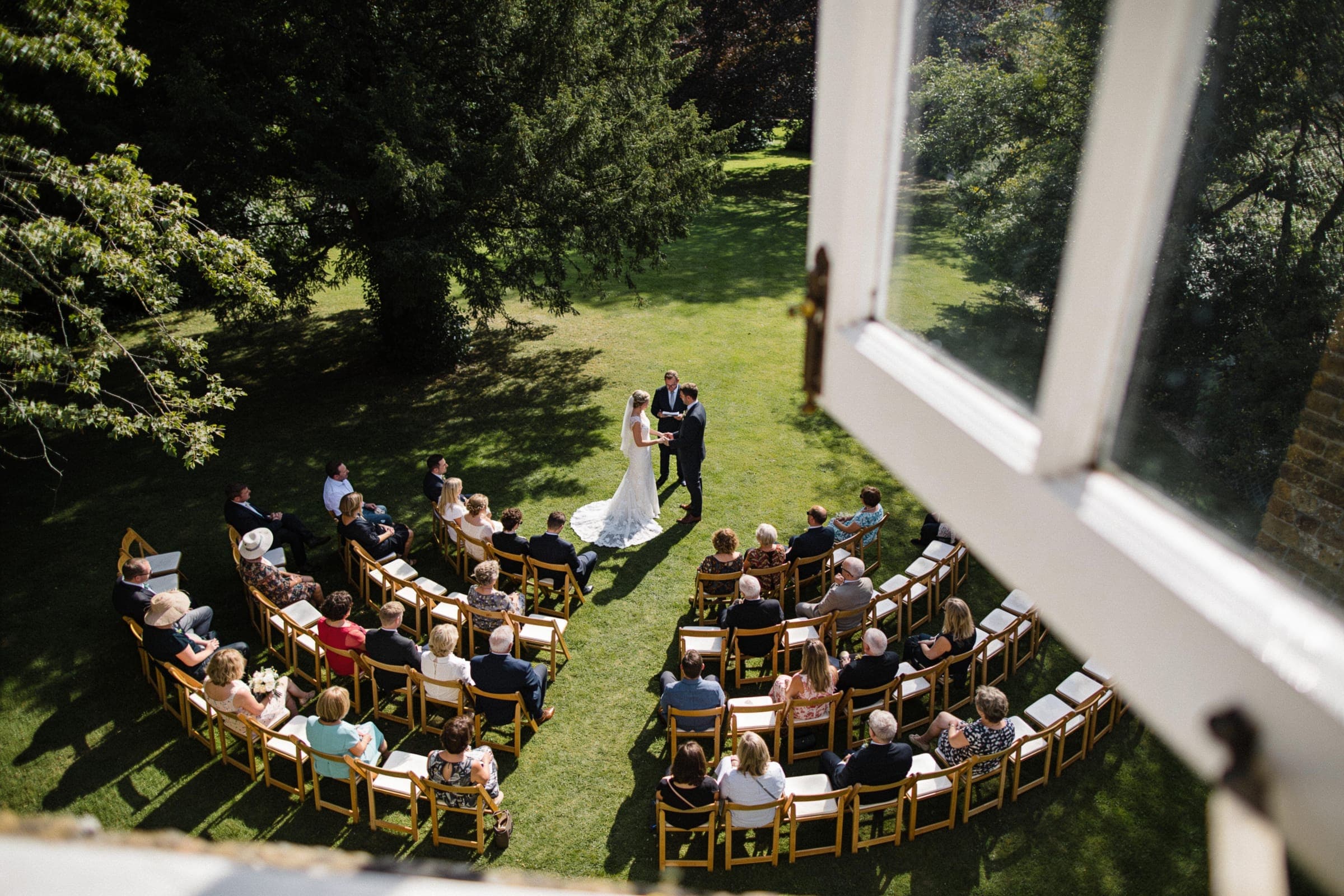 A garden ceremony seen from an upper window, with guests seated in curved rows around the couple.