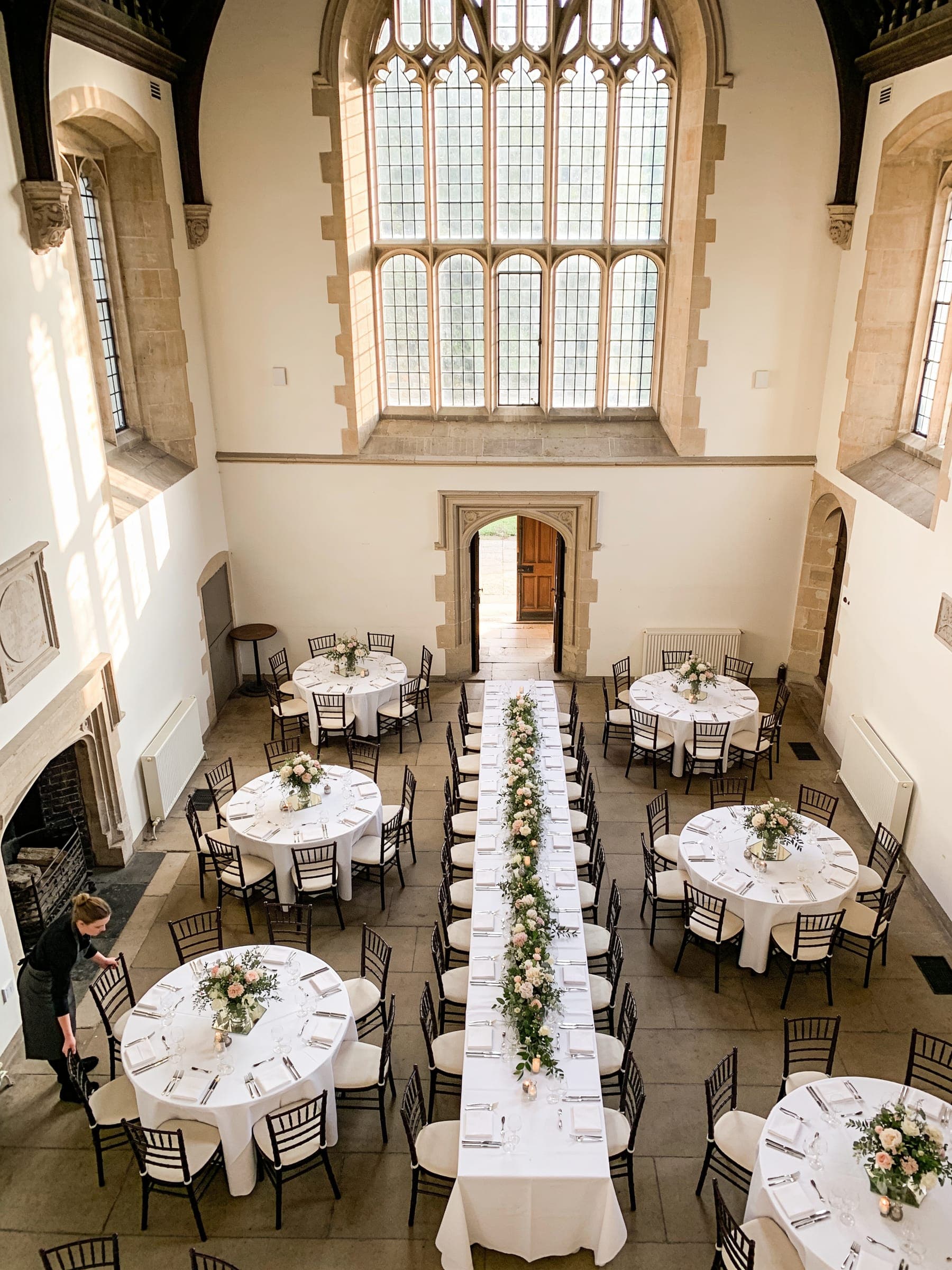 A high-ceilinged hall seen from above, set with one long central table and round tables around it, walkways clear between them.